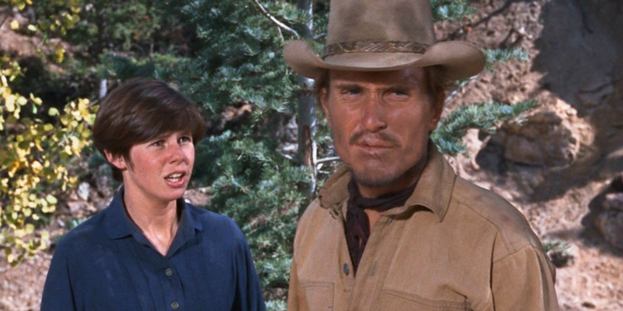 Robert Duvall standing in front of Kim Darby in the mountains in True Grit (1969)