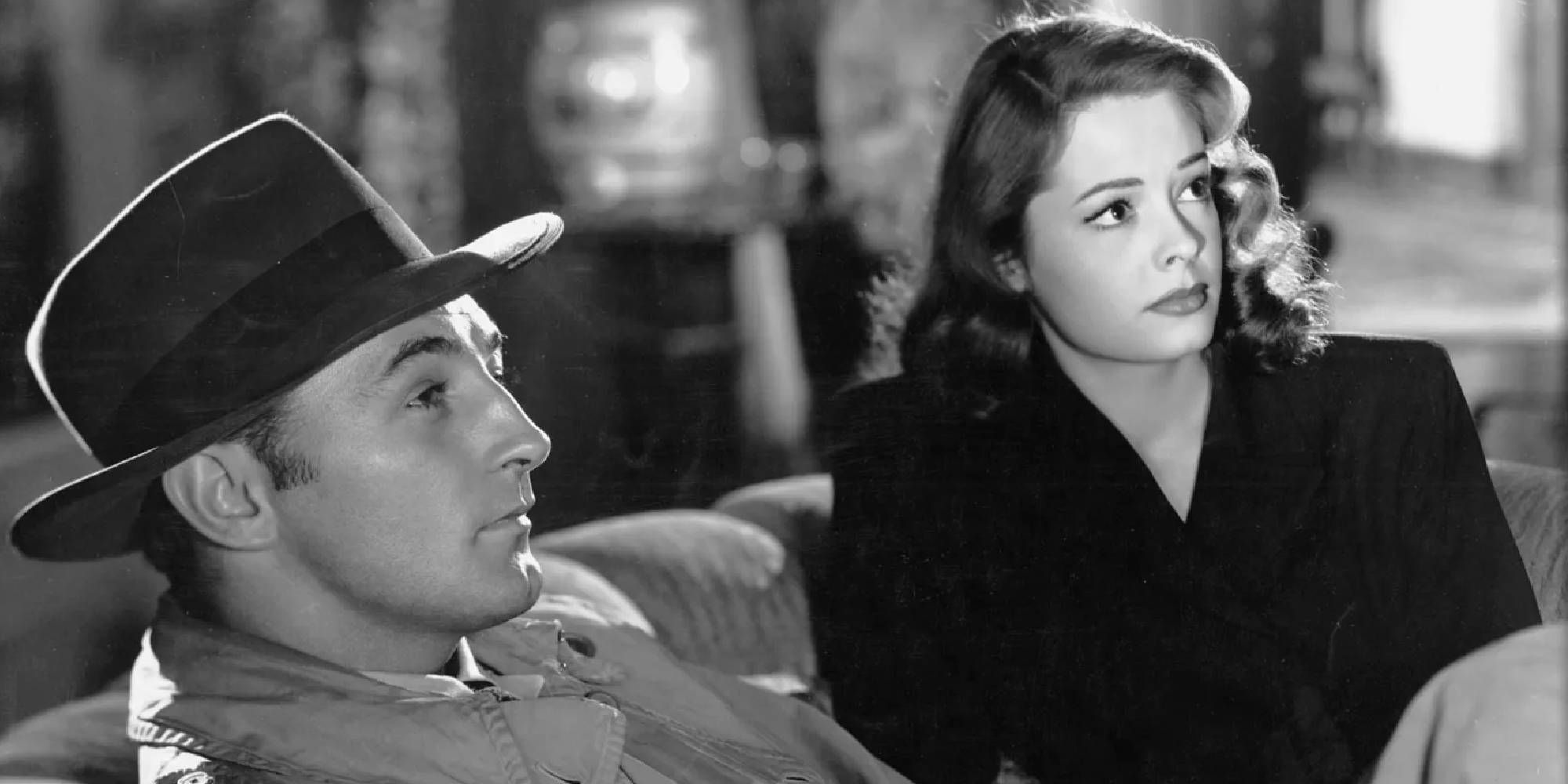 Robert Mitchum as Jeff Bailey and Jane Greer as Kathie Moffat sitting on a couch in Out of the Past