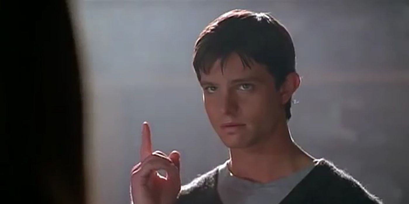 A young man holds his finger pointing into the air in a scene from Roswell.