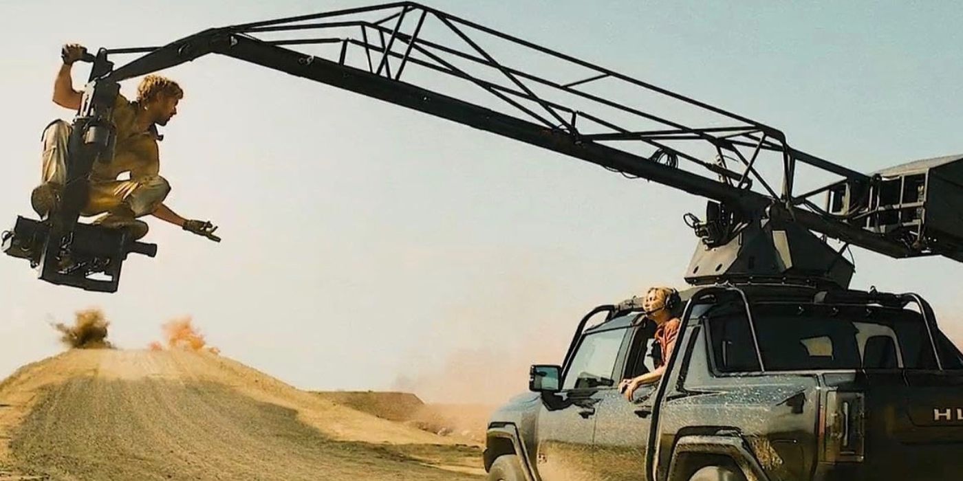 Ryan Gosling gestures to Emily Blunt from the end of a crane attached to the truck she is driving in The Fall Guy​​​​​​​.