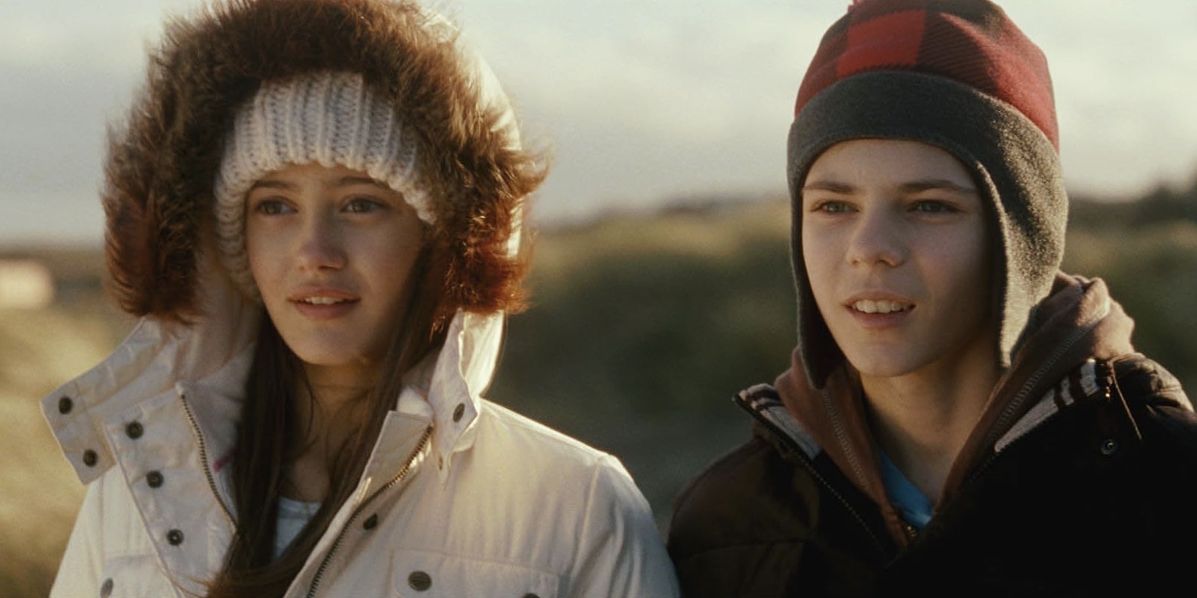 A young girl and boy looking intently ahead in the open field in Ways to Live Forever