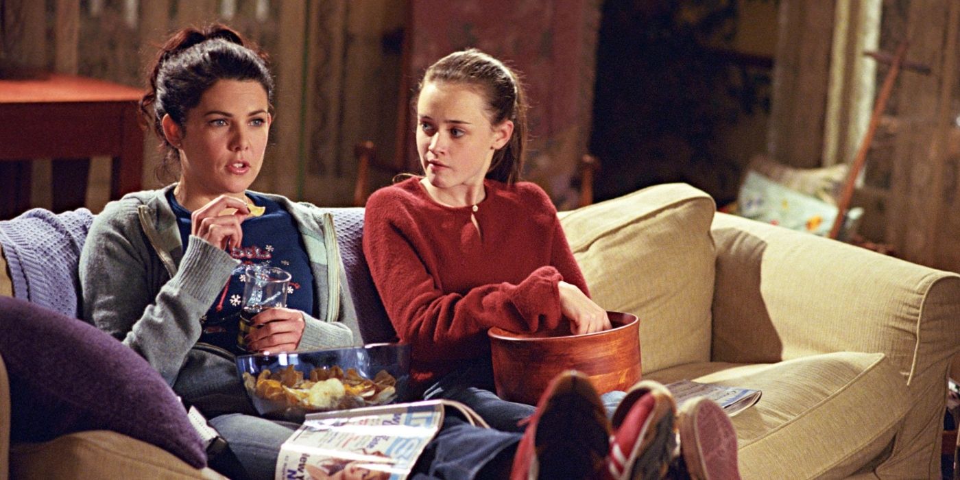 Lauren Graham and Alexis Bledel as Lorelai and Rory Gilmore, sitting on their couch eating snacks on Gilmore Girls