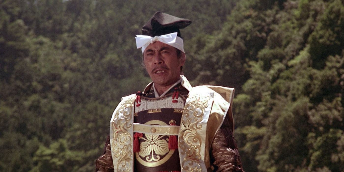 Toranaga (Toshiro Mifune) standing outside with a heavy grouping of trees a distance behind him and wearing golden, red, and brown armor in the 1980 Shogun