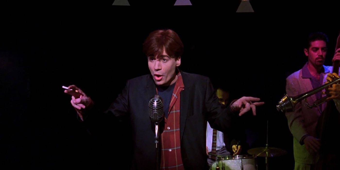 Mike Myers standing behind a mic holding a cigarette in one hand, both hands outstretched, mouth open in a scene from So I Married An Axe Murderer.