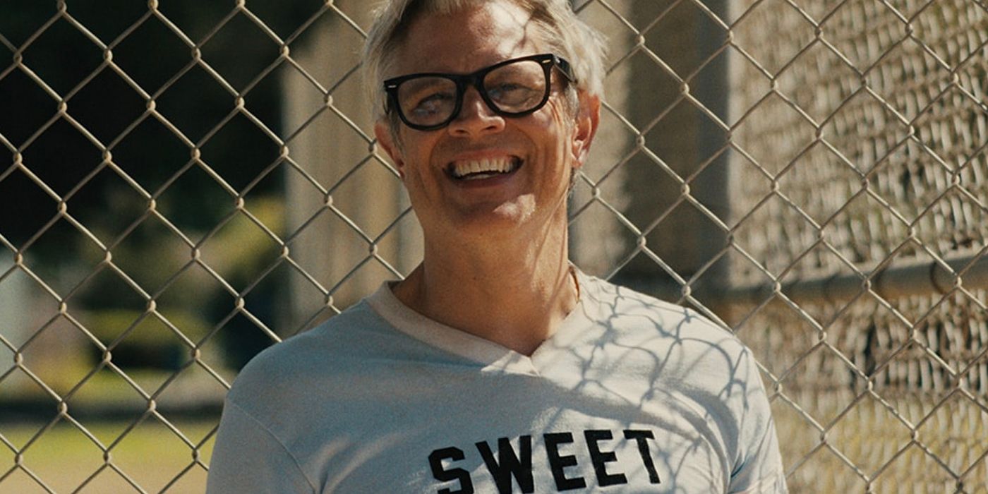 Johnny Knoxville smiling in front of a chain link fence in Sweet Dreams