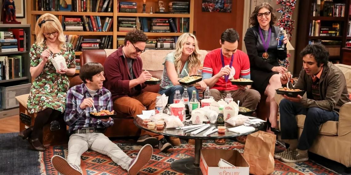 The full main cast of 'The Big Bang Theory' sitting in the living room eating takeaway.