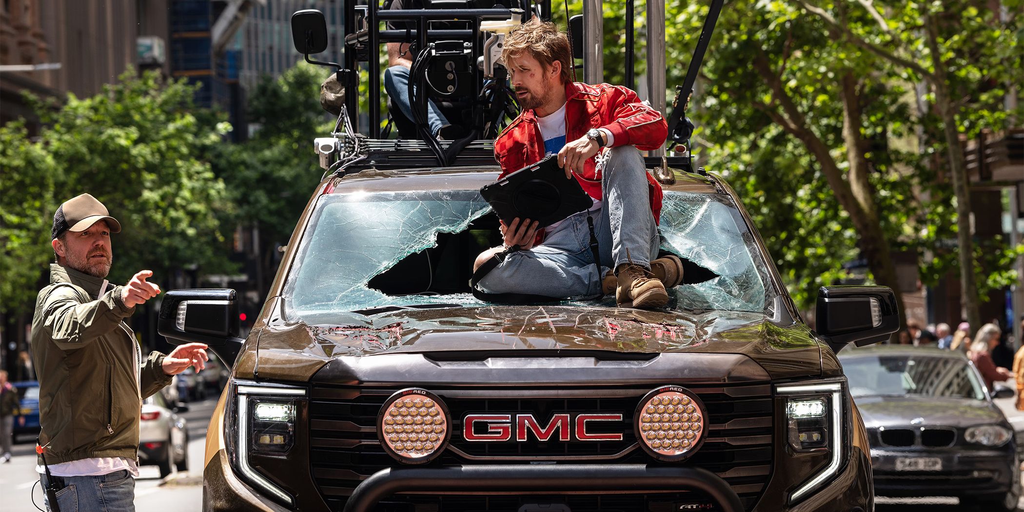 Ryan Gosling sitting on the hood of a car while David Leitch explains something for The Fall Guy