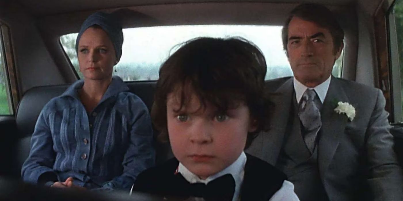 Damien (Harvey Spencer Stephens) in the foreground looks angry while Robert (Gregory Peck) and Katherine (Lee Remick) sit behind.