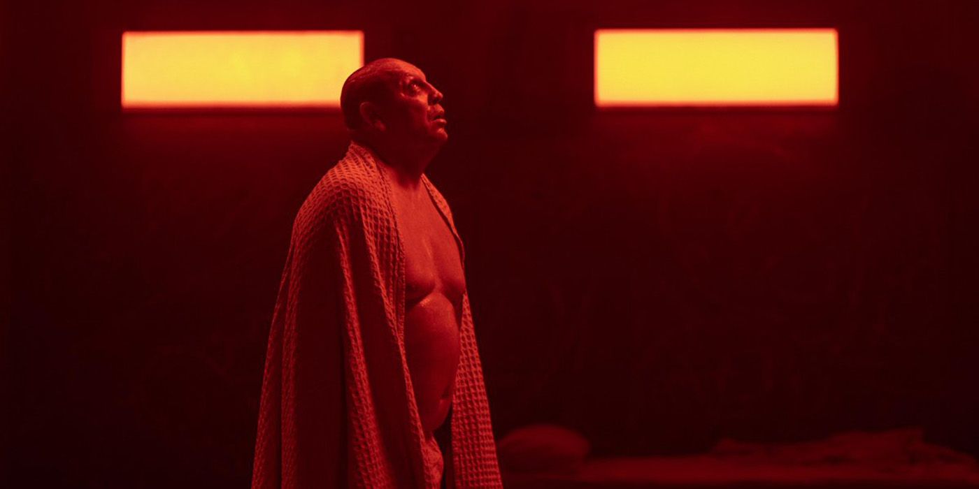 Hovik Keuchkerianm shirtless and wrapped in a blanket looking upward while bathed in red light in The Platform 2