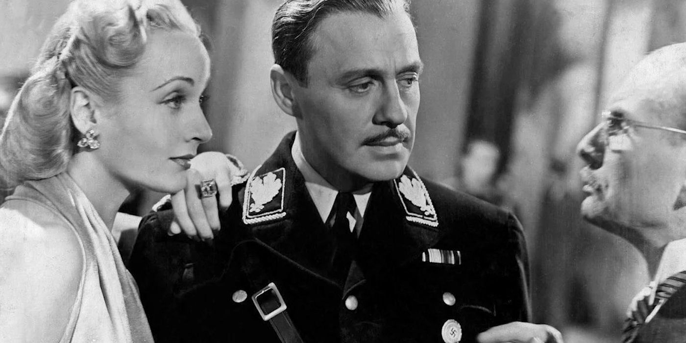 A man in a military uniform and a woman in a nice dress talk to another person in To Be or Not to Be.