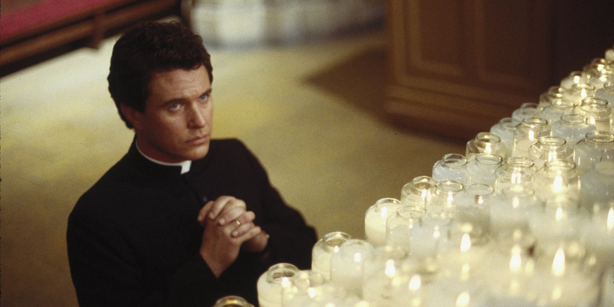 Tom Berenger kneeling against a candle memorial inside a church in Last Rites (1988)