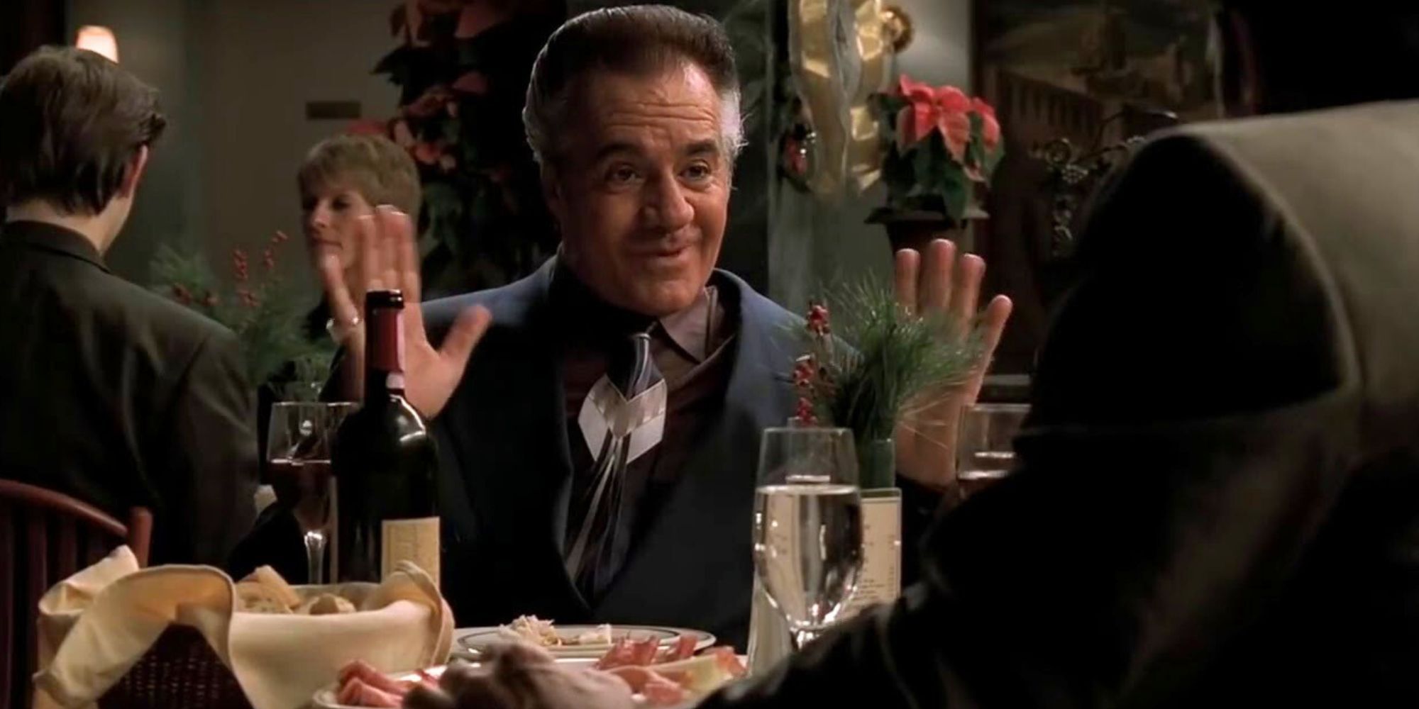 Tony Sirico as Paulie Walnuts sitting at a dinner table with his hands up in The Sopranos