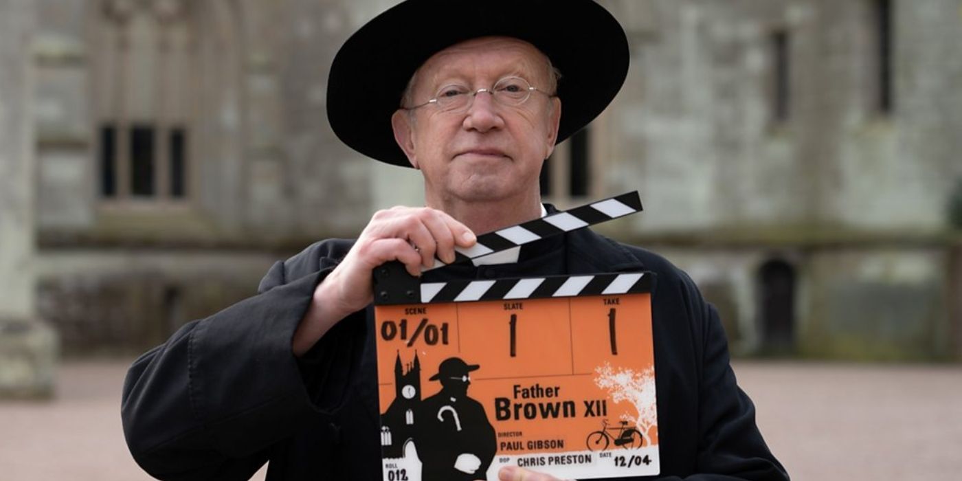 Mark Williams as Father Brown holding an orange film clapper at the start of Season 12