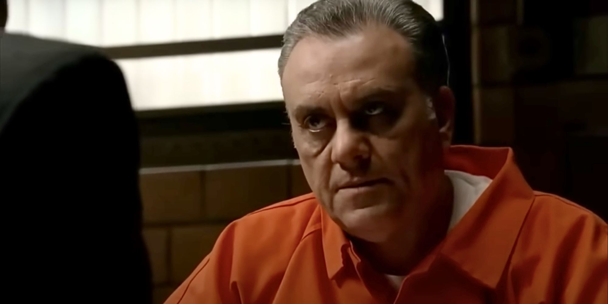 Vincent Curatola as Johnny Sack wears a prison jumpsuit & sits at a table in The Sopranos