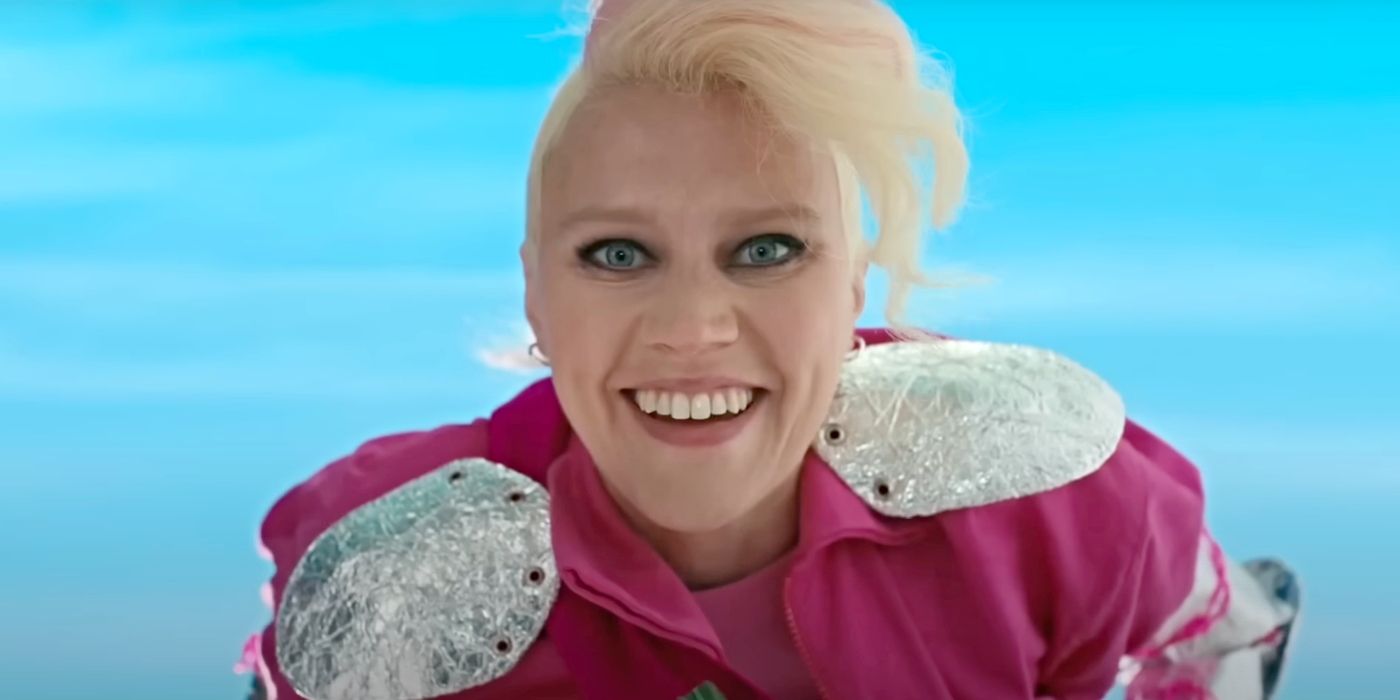 Kate McKinnon as Weird Barbie, staring intensely into the camera and smiling in Barbie