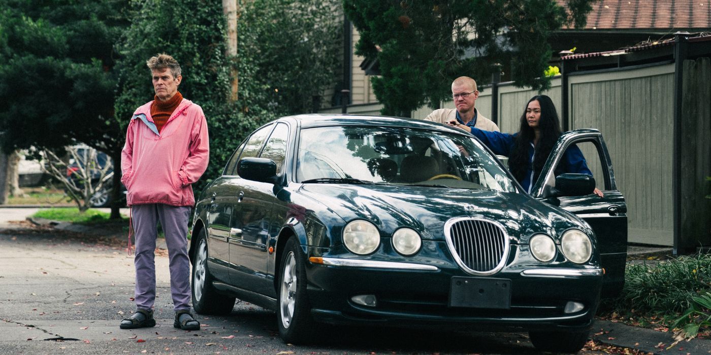 Willem Dafoe, Jesse Plemons, and Hong Chau standing outside of a car in Kinds of Kindness.