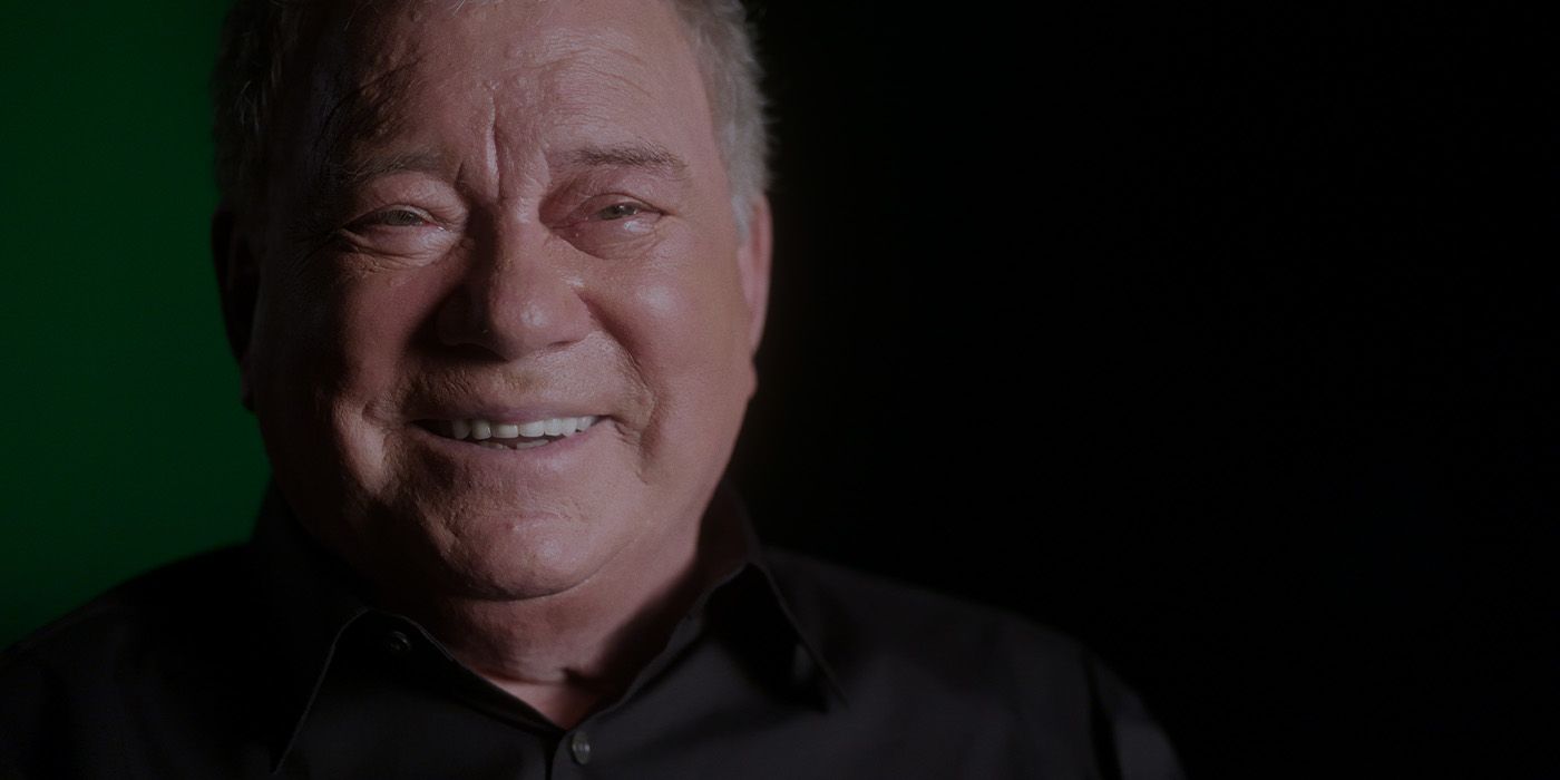 William Shatner facing the camera and laughing against a dark backdrop