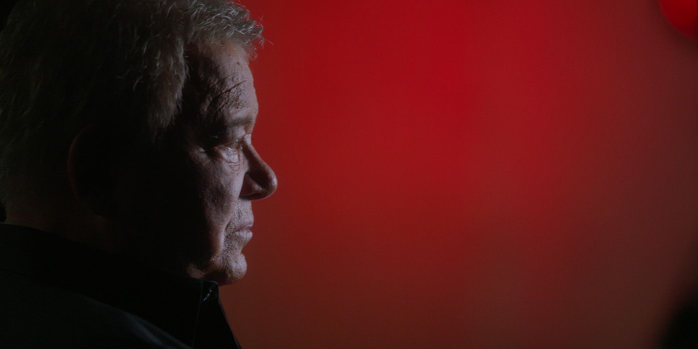 The profile of William Shatner looking to the right against a red backdrop