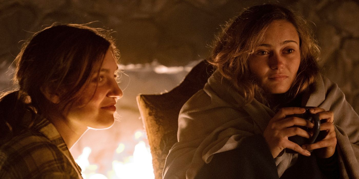 Ella Purnell as Jackie and Sophie Nélisse as Shauna sit in front of a fireplace in Yellowjackets.