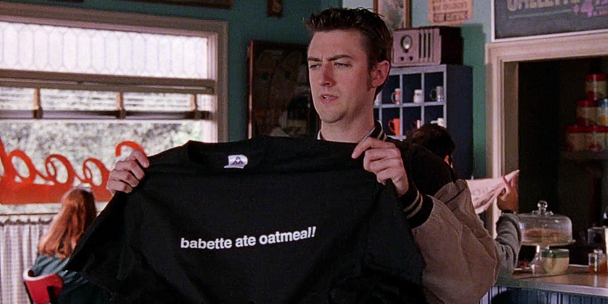 Kirk Gleeson holding a 'Babette ate oatmeal!" shirt in Gilmore Girls