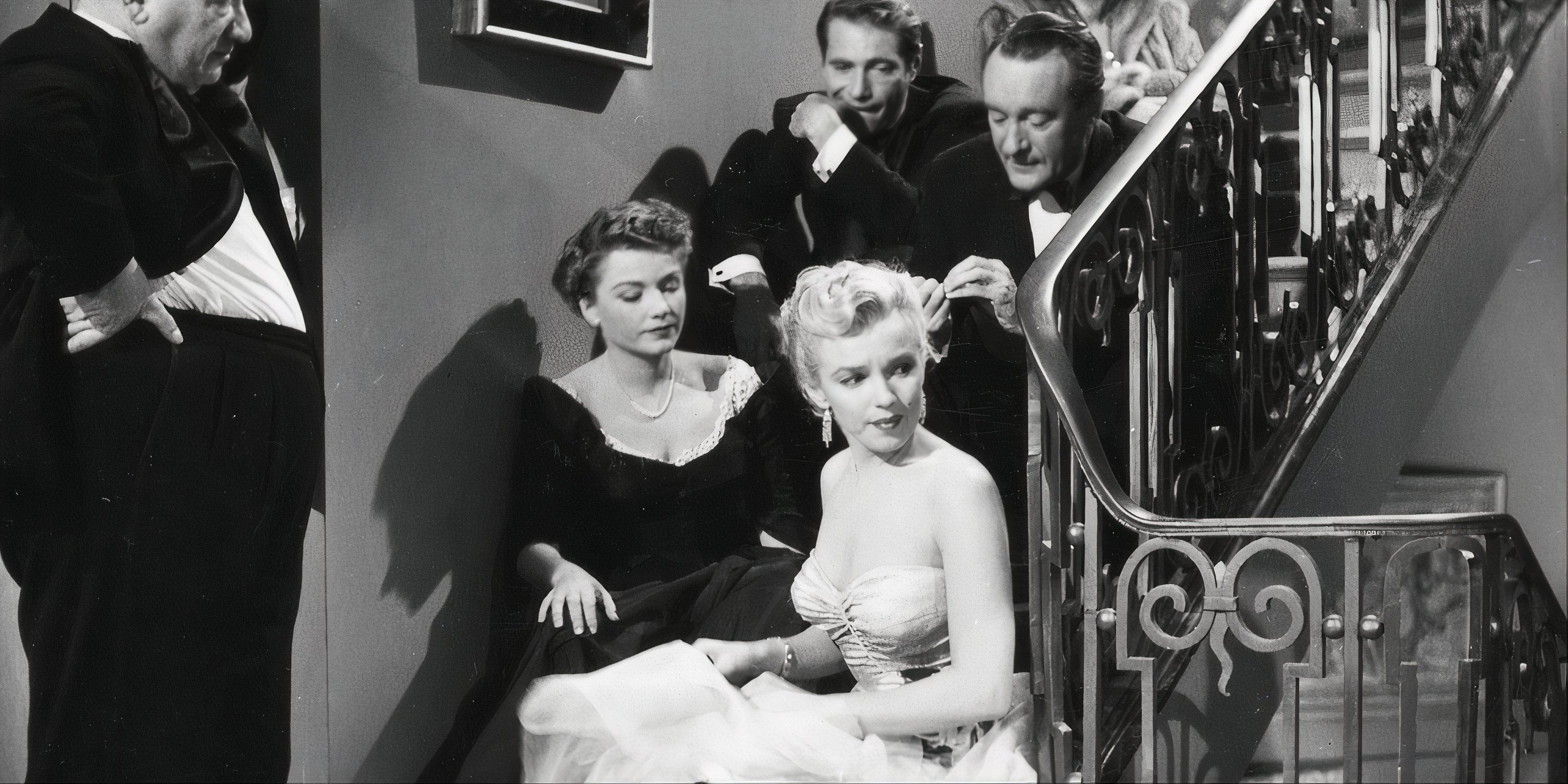 Marilyn Monroe as Miss Casswell sitting on the stairs looking worried with several people behind her also sitting in All About Eve