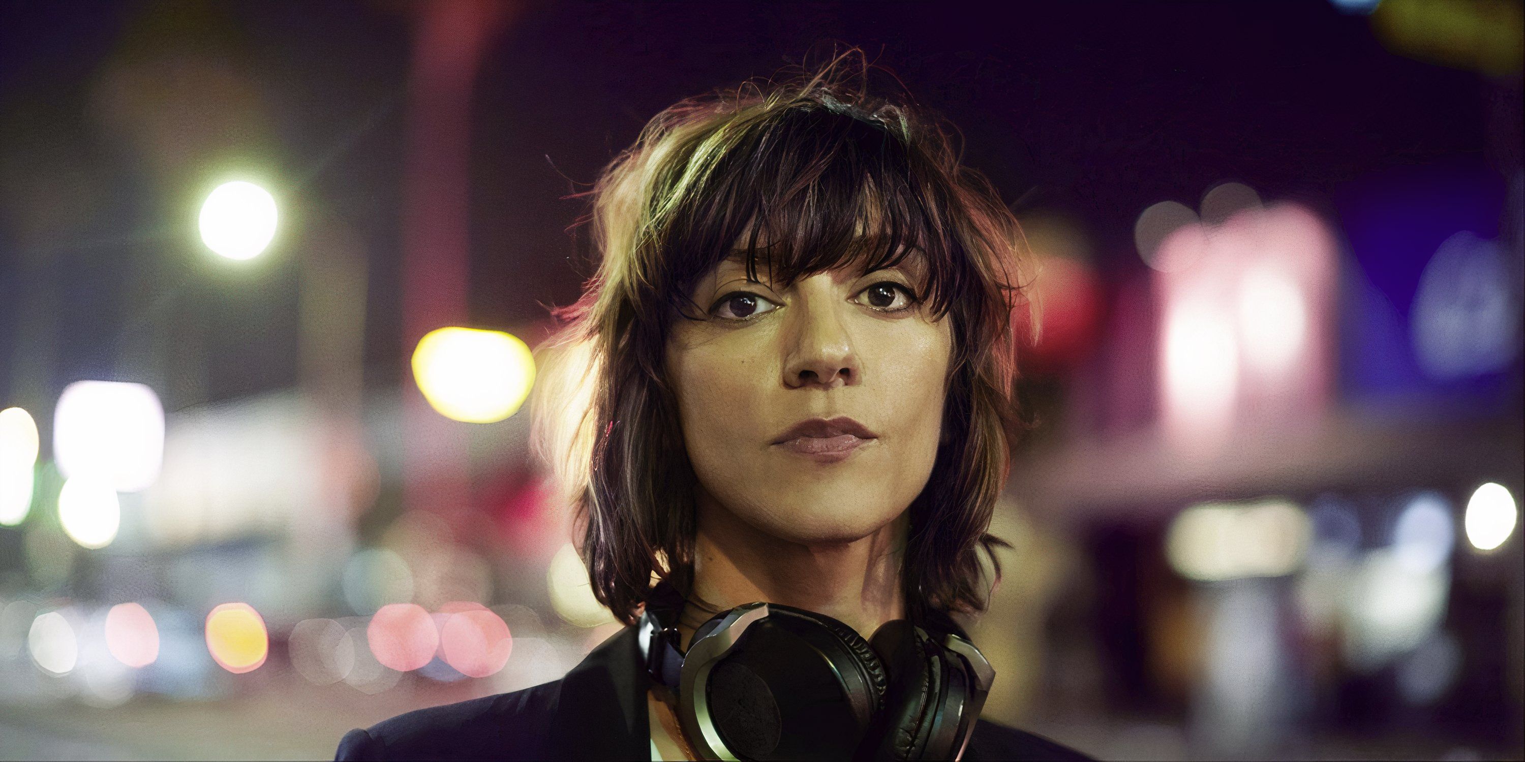 Ana Lily Amirpour standing in the street with headphones around her neck.