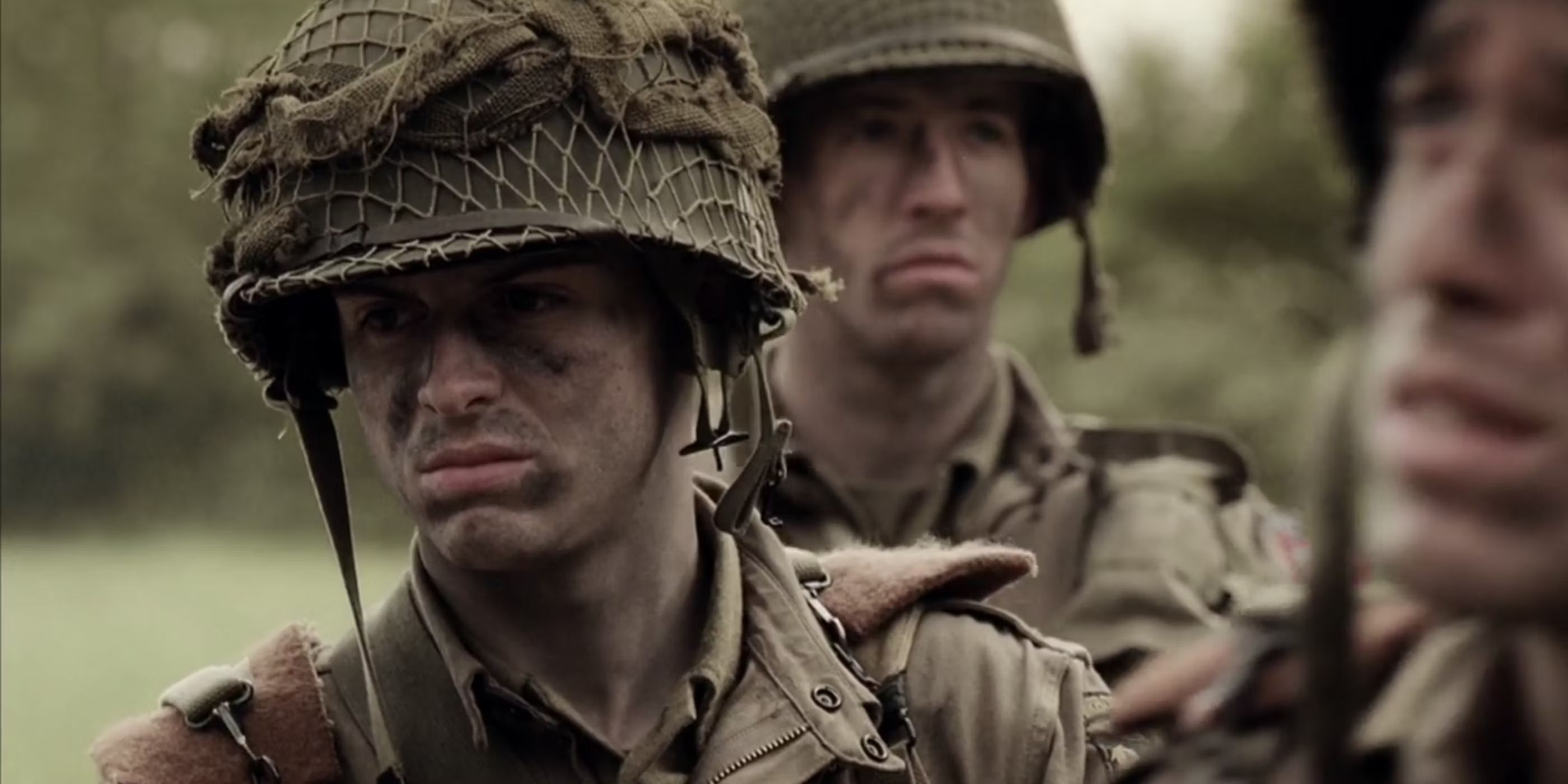 Private John "Cowboy" Hall (Andrew Scott) stands in his army gear with face camo alongside his fellow soldiers in Band of Brothers
