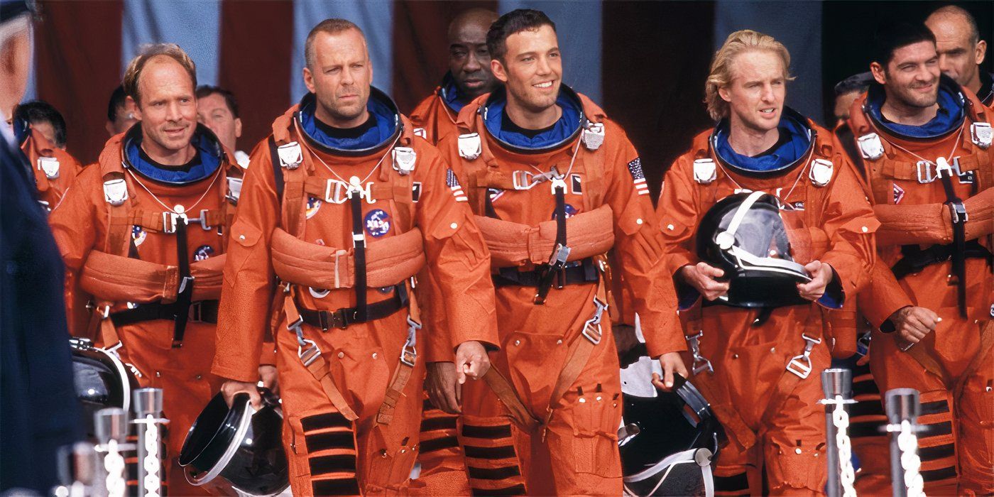 The cast of Armageddon walking in their orange spacesuits smiling at onlookers off-camera