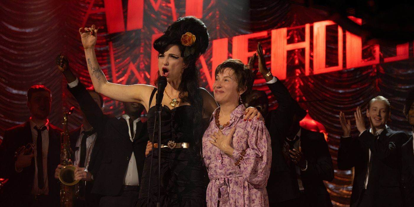 Marisa Abela on stage as Amy Winehouse raising her right arm in the air with her left arm around Juliet Cowan as Janis Winehouse.