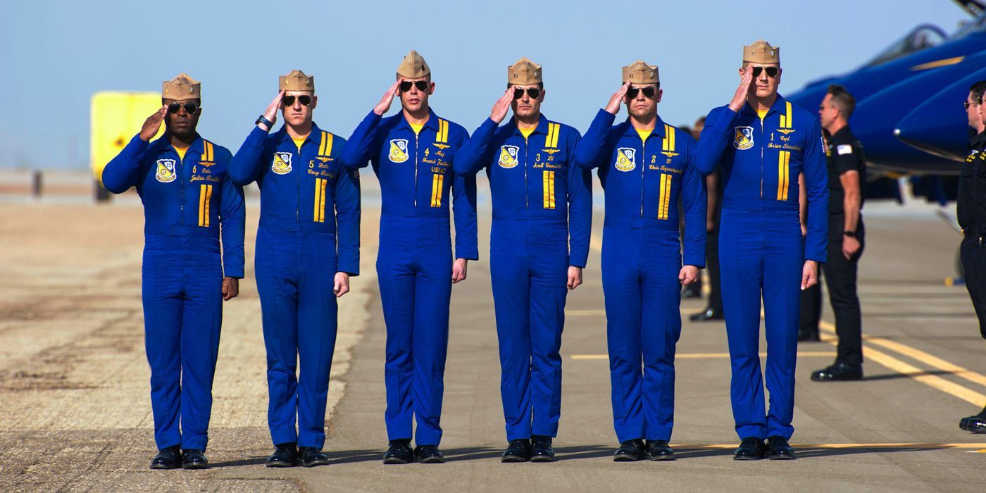 Six Blue Angel pilots standing on the runway in uniform, saluting.