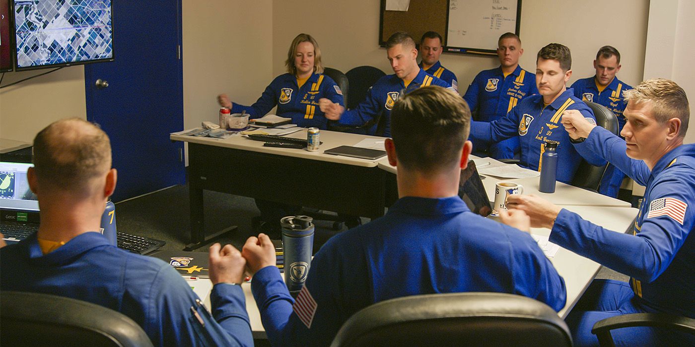 The Blue Angels sit in a command center at desks fist bumping each other
