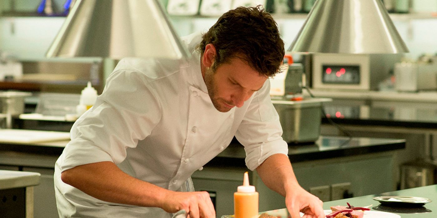 Bradley Cooper as chef Adam Jones concentrating while assembling a dish in Burnt