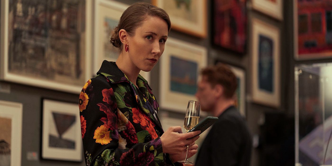 A woman standing in an art gallery wearing a floral dress and holding a glass of champagne looking at someone sneakily in a scene from Chloe.