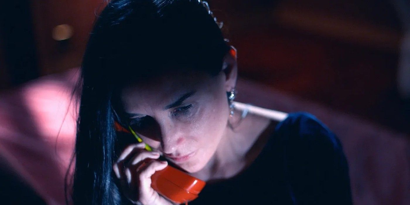 Demi Moore talks on the phone while cast in shadow in a still from The Substance. 