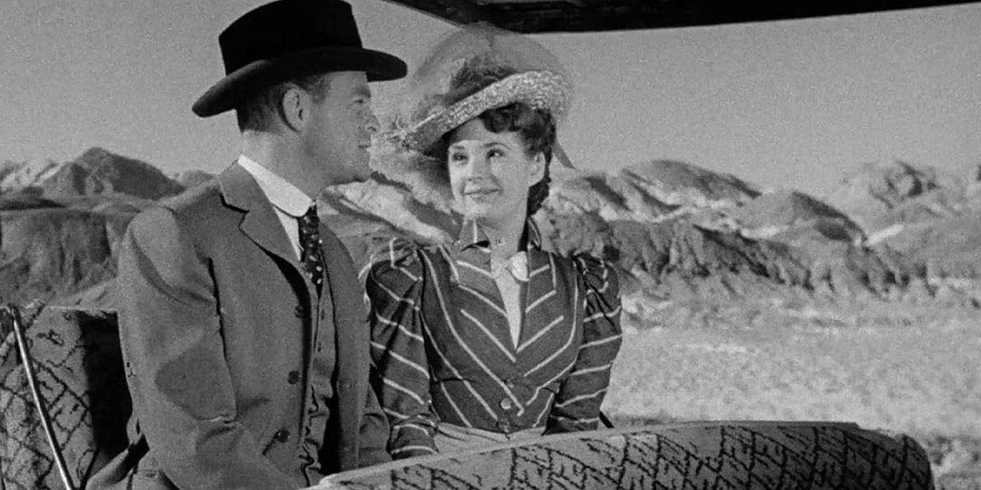 A couple in period western clothes smile at each other with mountains behind them in Death Valley Days.