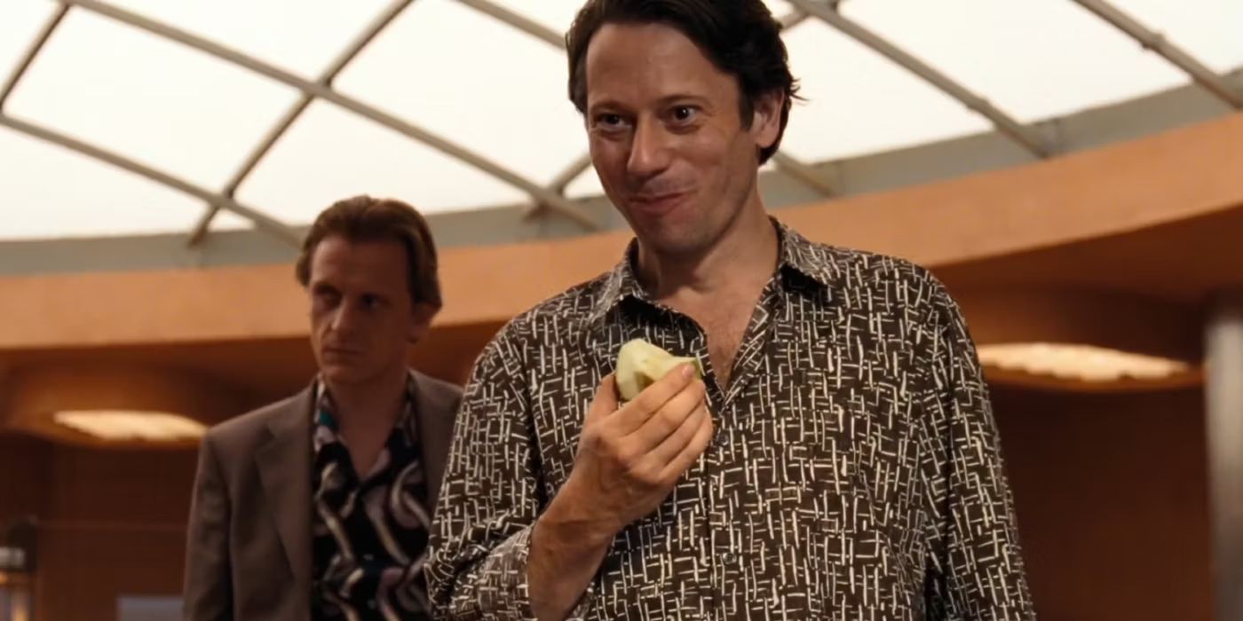 Dominic Greene (Mathieu Amalric) eats an apple in the middle of an atrium, flanked by a henchman