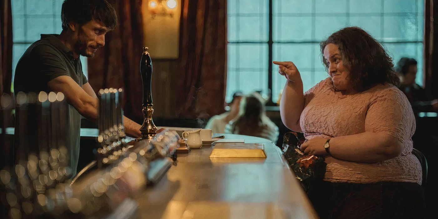 A woman sits at a bar and points playfully to the male bartender in Baby Reindeer. 