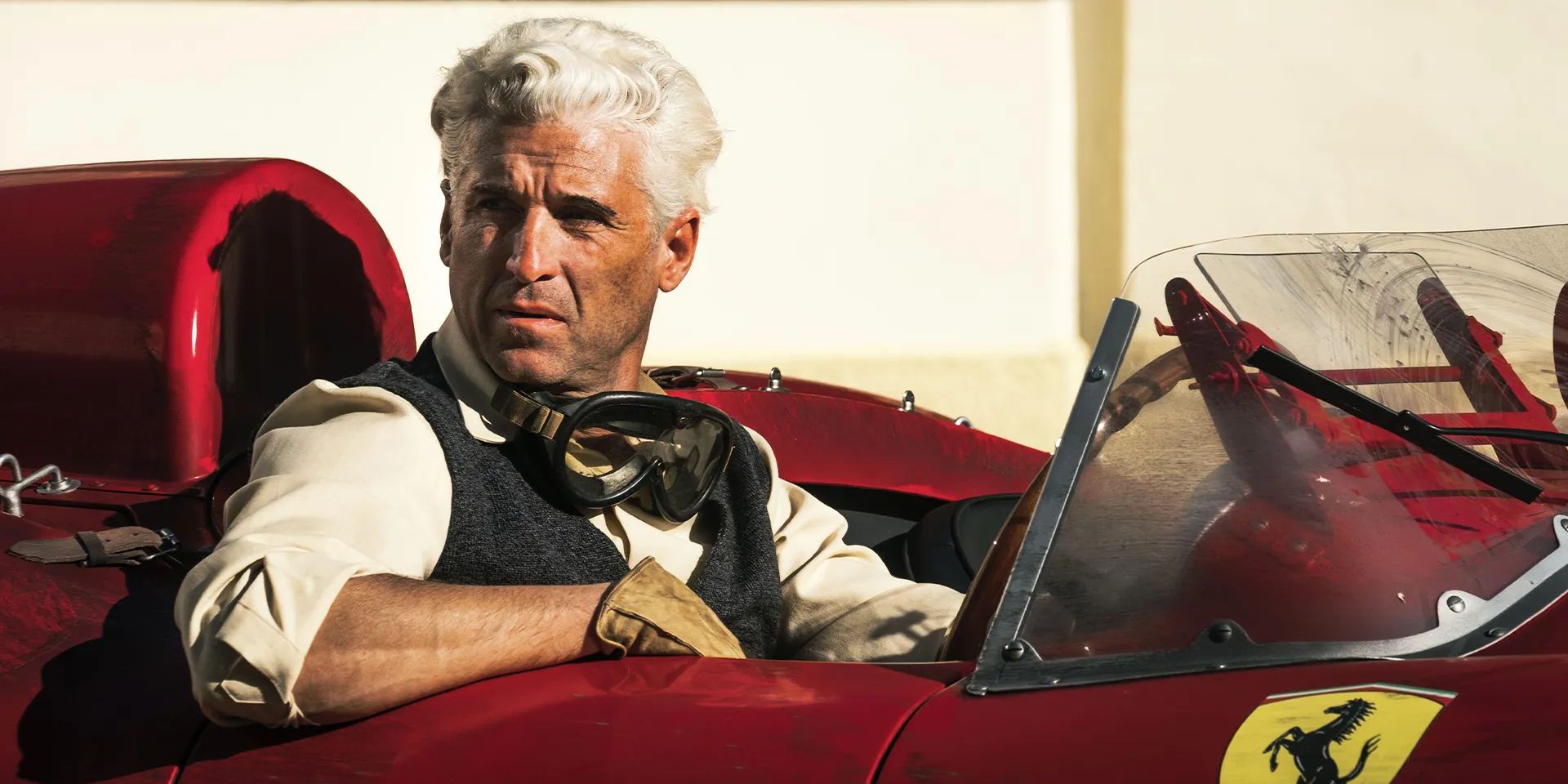 Patrick Dempsey sits in a red ferrari, wearing racing gear in Michael Mann's 'Ferrari'