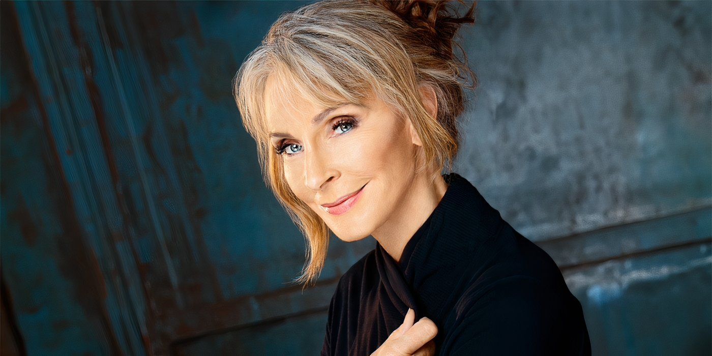 Gates McFadden in a black top in front of a blue wall in a headshot for InvestiGates