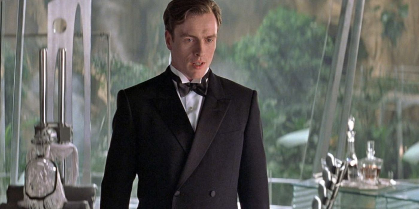 Toby Stephens as Gustav Graves stands in a glassed-in room in a tuxedo