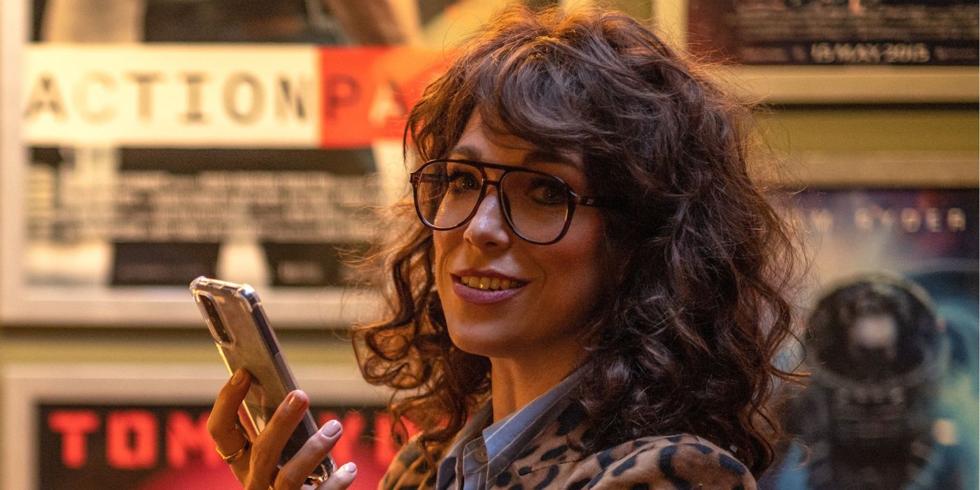 Hannah Waddingham wearing large eyeglasses, smirking, and smirking while holding up her iPhone as Gail.
