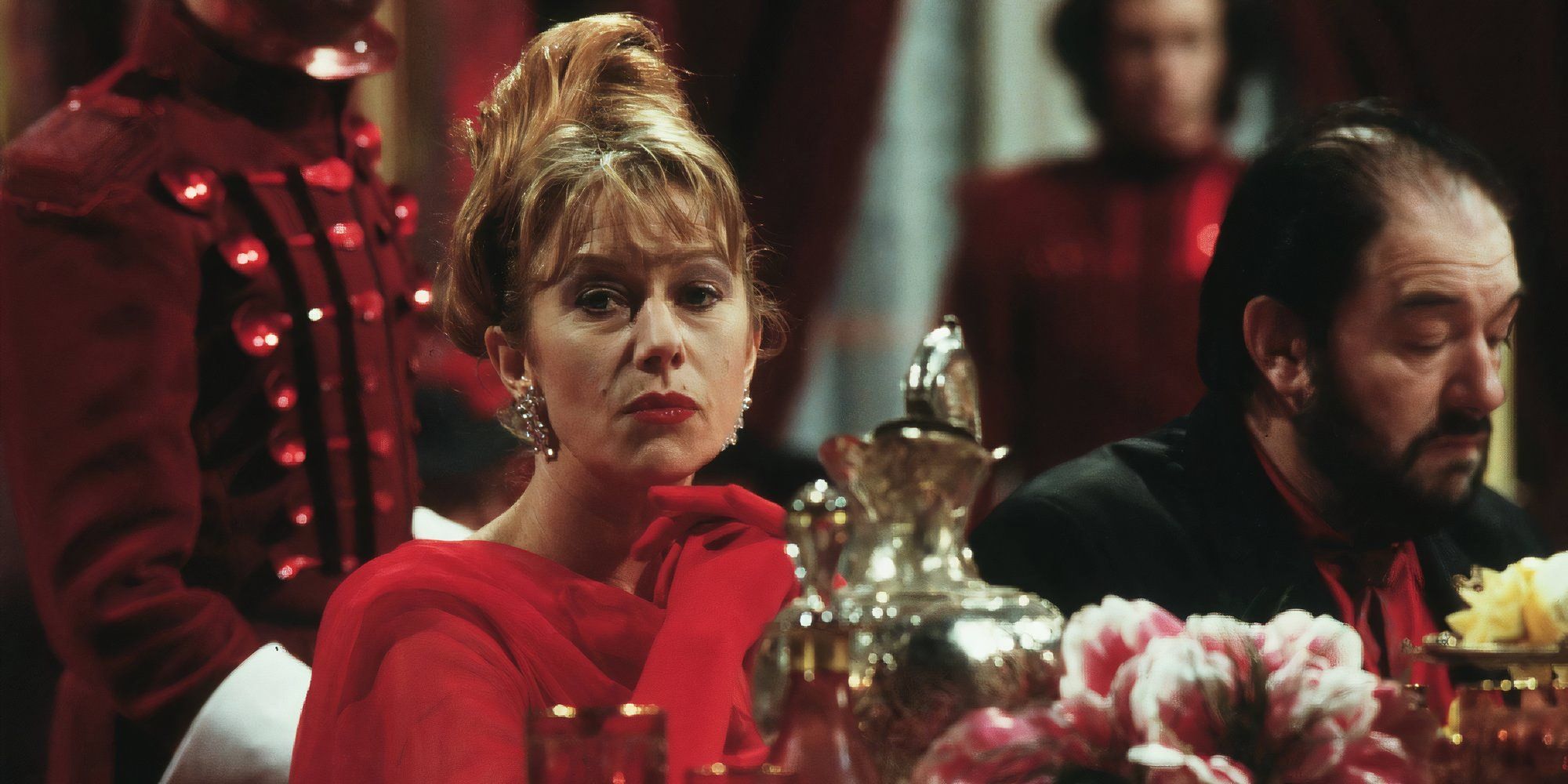 Helen Mirren as Georgina Spica wearing red while sitting at the table in The Cook, the Thief, His Wife & Her Lover.