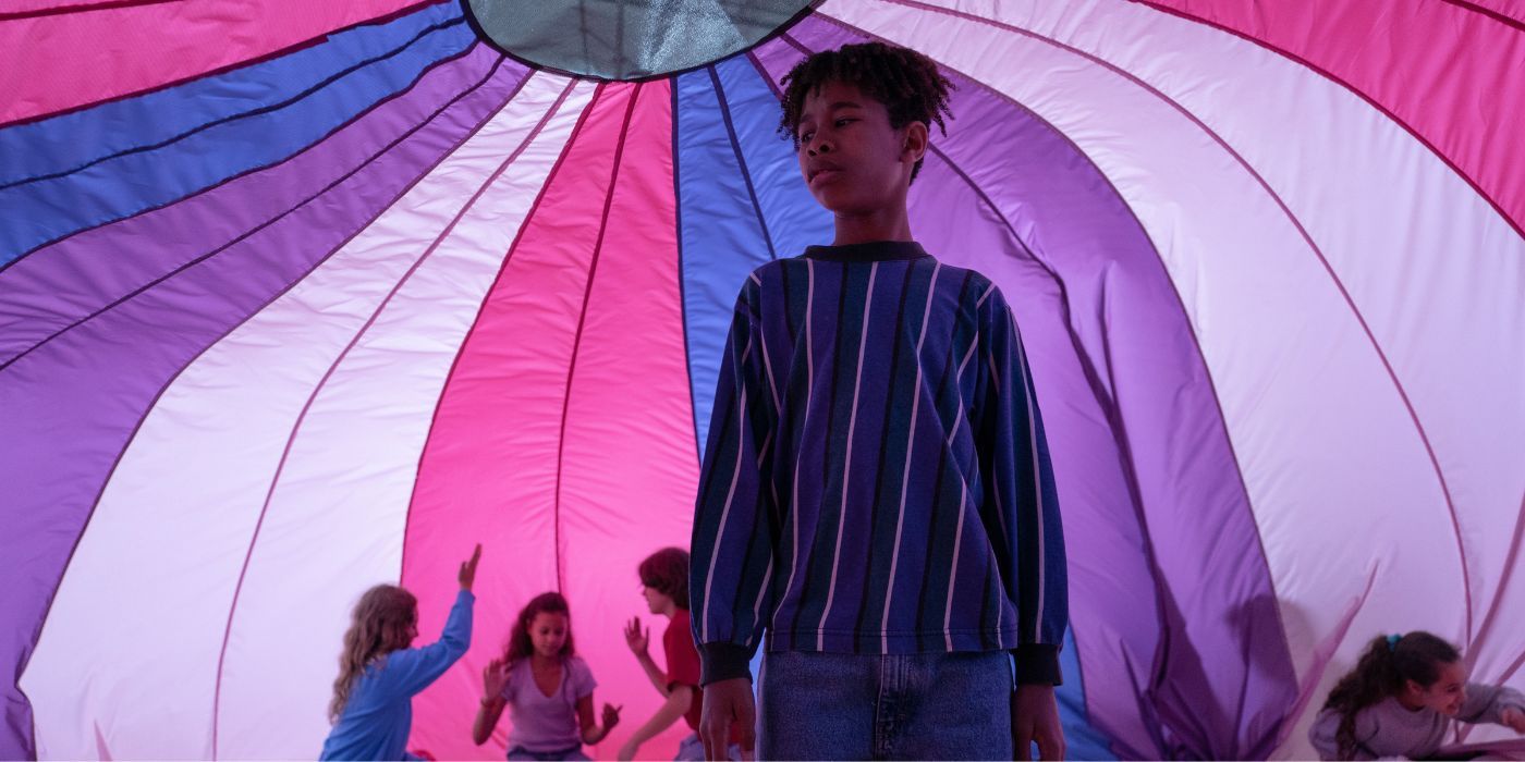 Ian Foreman standing under a parachute in the colors of the bi flag, while other children dance around him.