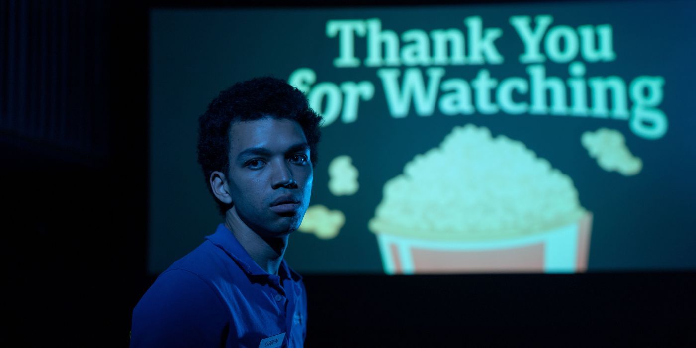 Justice Smith standing up in a dark movie theater with a 