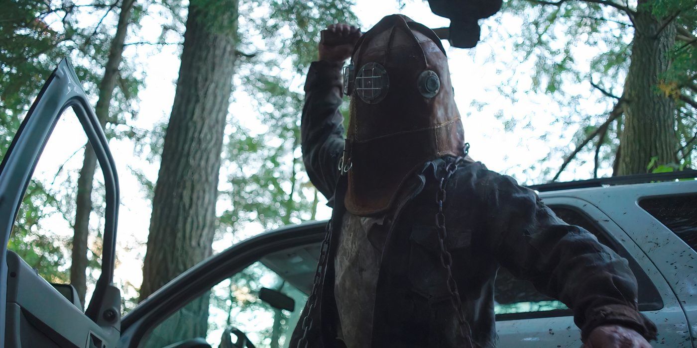 The masked killer standing outside the car, wielding an axe.