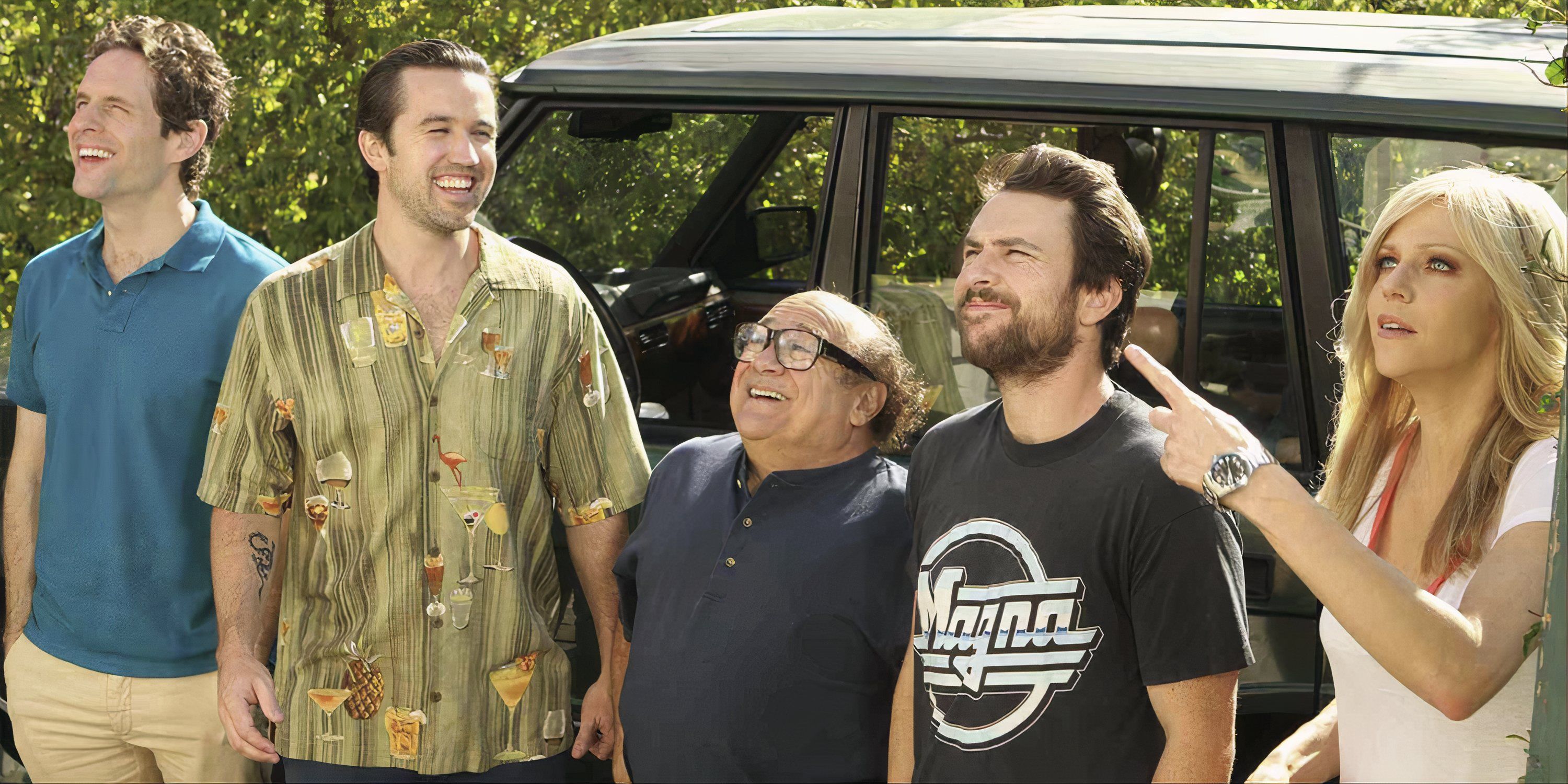 The cast of It's Always Sunny in Philadelphia standing in front of a car looking and smiling at something off-camera.
