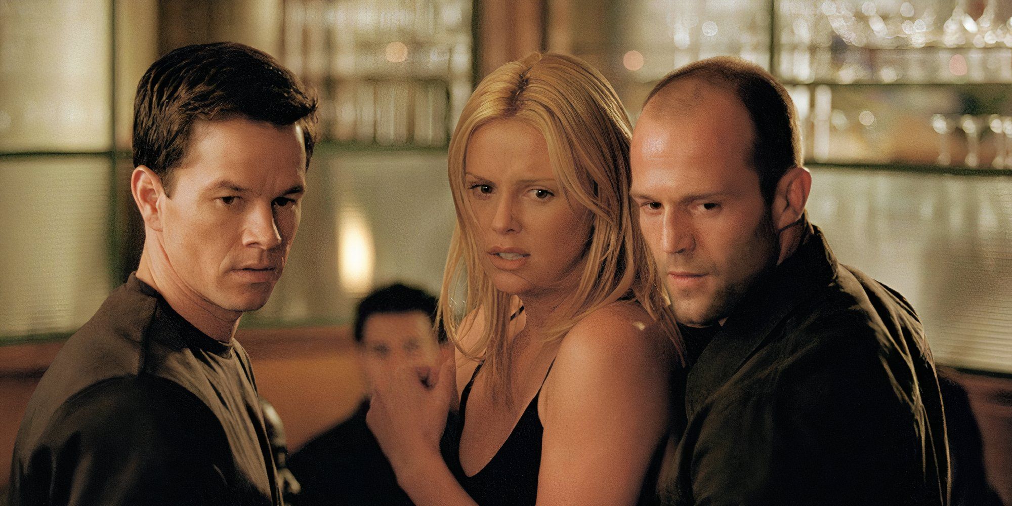 Marl Wahlberg as Charlie Croker, Jason Statham as Handsome Rob and Charlize Theron as Stella Bridger in The Italian Job all standing next to each other at a bar.