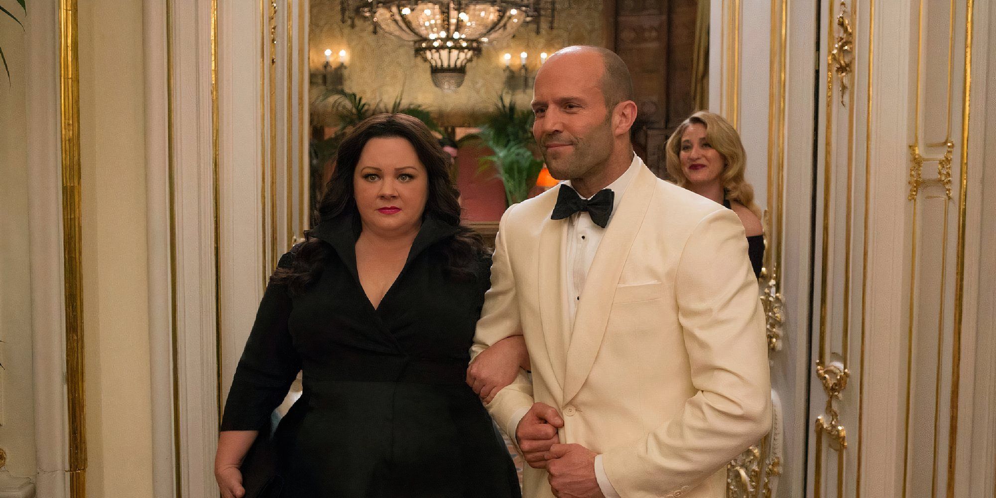 Melissa McCarthy as Susan Cooper holding onto Jason Statham as Rick Ford as the two walk side by side at a party in Spy.