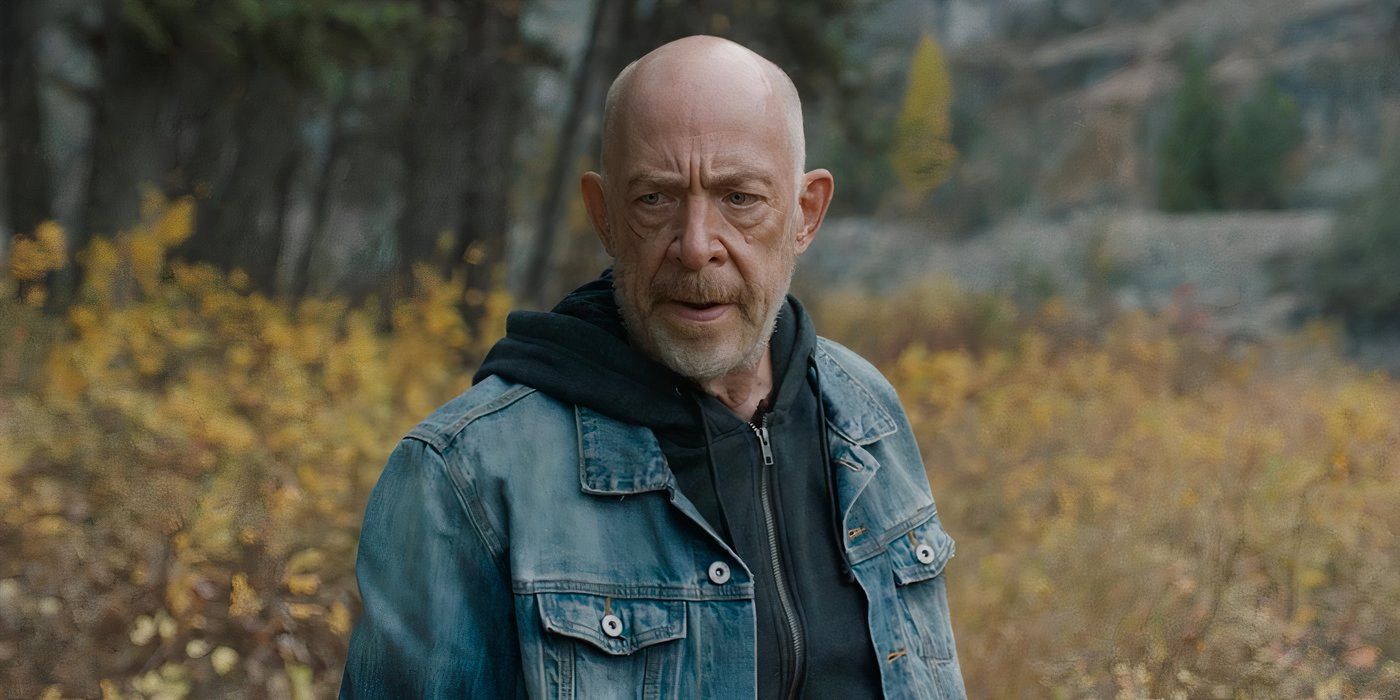 J.K. Simmons standing in a marsh looking tough while wearing a jean jacket.