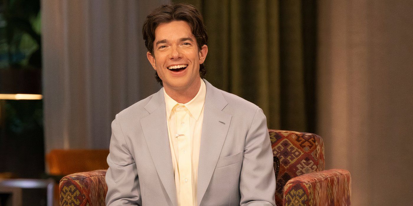 John Mulaney smiling in a suit while sitting in a leather chair in Everybody's in LA.